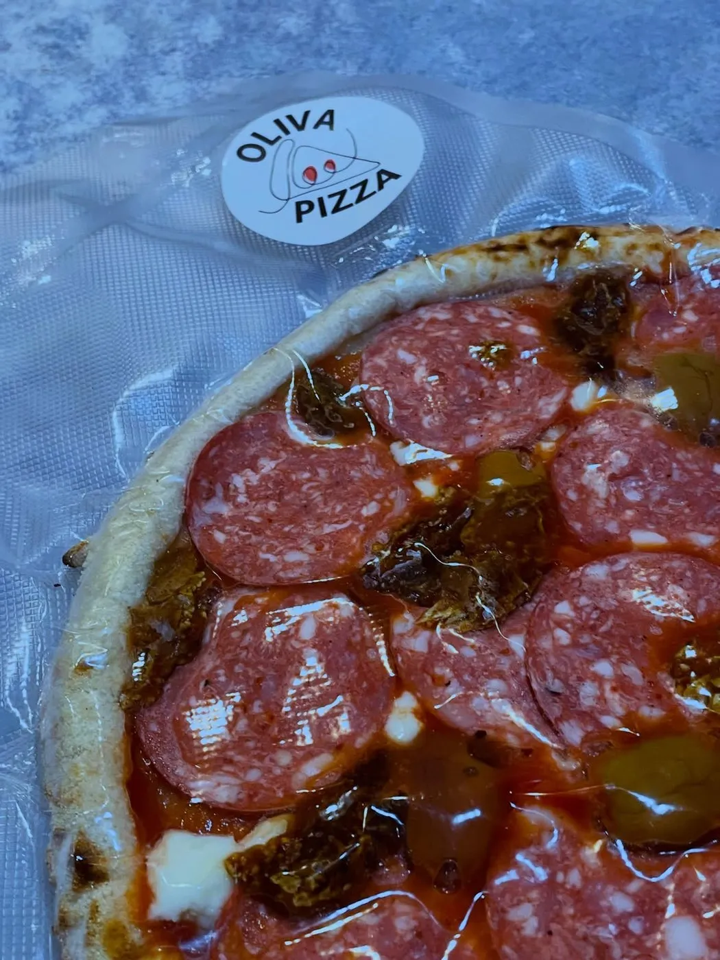 A Bake at Home pizza vacuum sealed, with the round Oliva Pizza sticker