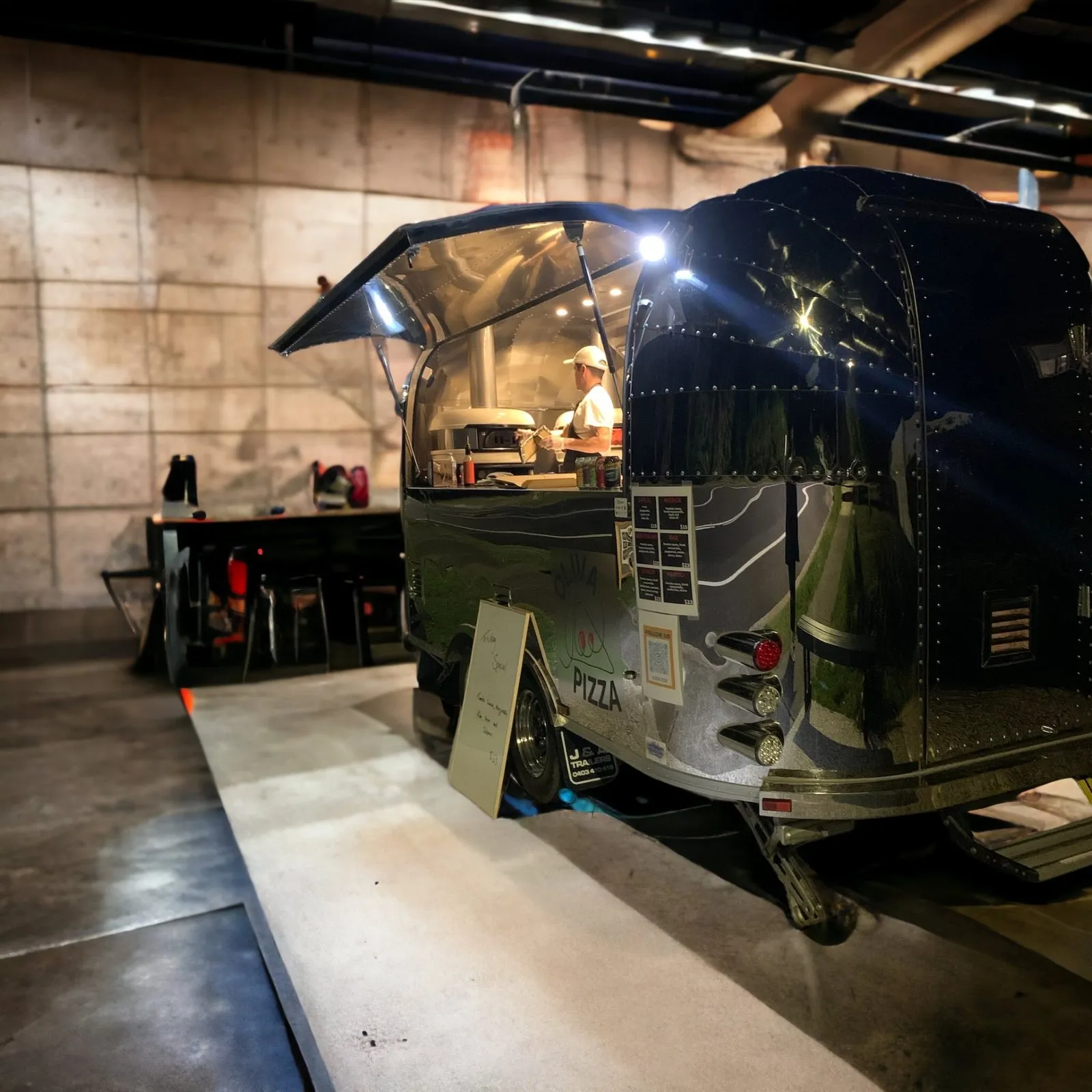 The trailer parked inside a brewery, hatch open, tables beside it